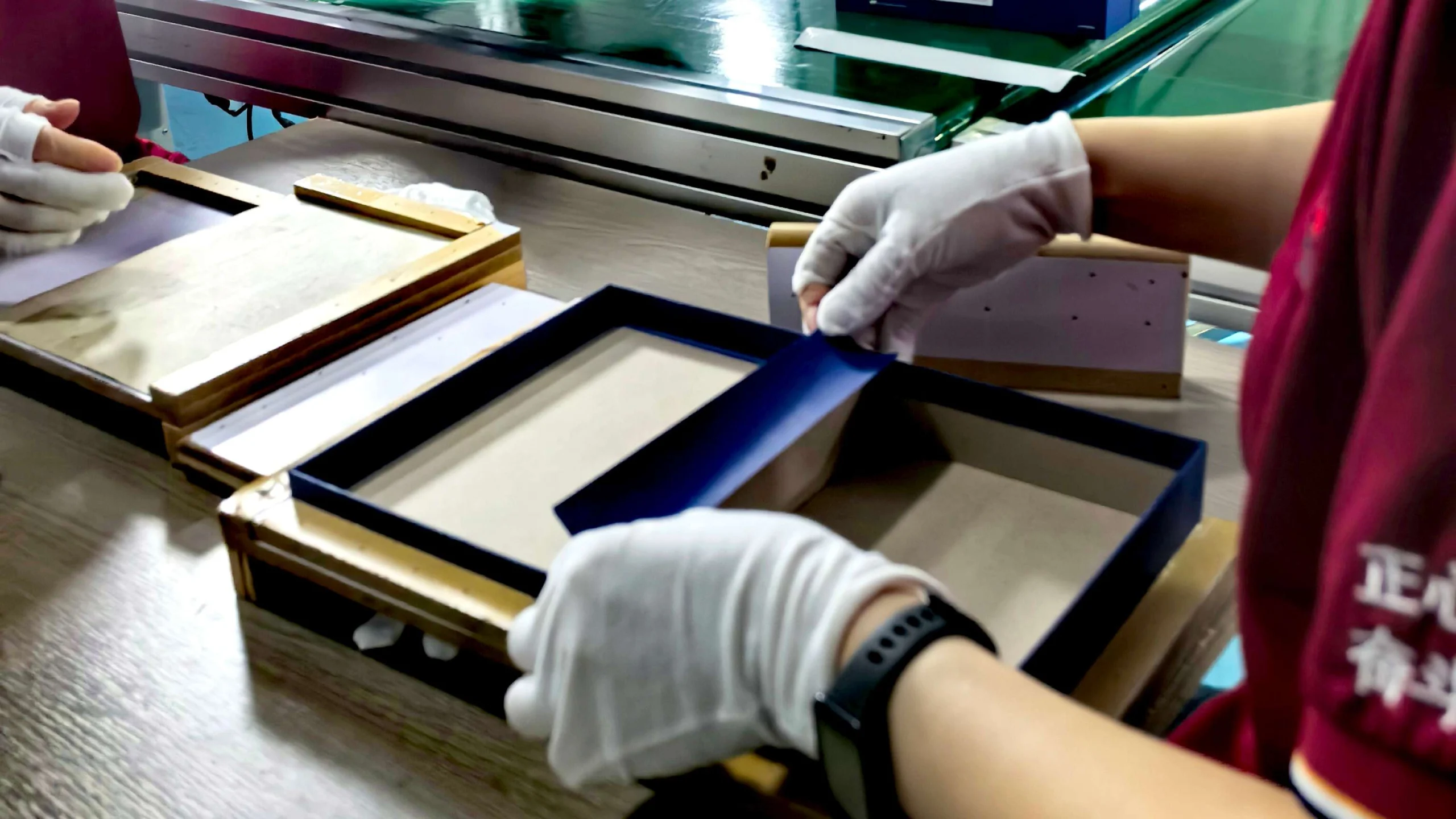 Production worker manually wrapping and assembling custom rigid boxes